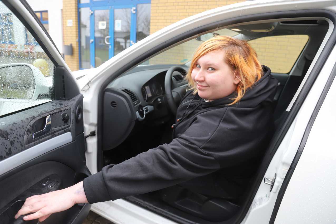 Eine junge Frau sitzt am Steuer eines Autos und zieht die Tür des Fahrzeuges zu.